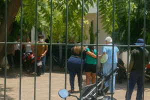 Familiares e profissionais de saúde em frente ao portão de uma escola estadual, após atentado no Ceará, sob árvores e com motocicletas próximas. Imagem restaurada por inteligência artificial.
