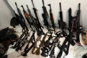 Arsenal de fuzis apreendido durante megaoperação policial no Rio de Janeiro, exibido em chão de quartel ou delegacia, com armas alinhadas. Imagem de reprodução jornalística da Agência Na Escuta, via BACCI Notícias.