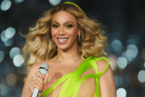 Beyoncé sorrindo no palco com vestido verde e microfone em mãos. Imagem adaptada por inteligência artificial.