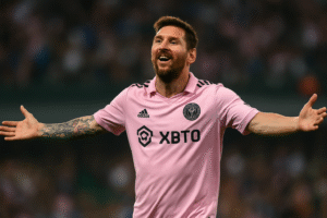 Imagem gerada por inteligência artificial retratando Lionel Messi comemorando um gol com os braços abertos em campo, usando o uniforme rosa claro do Inter Miami, em estilo fotográfico realista.