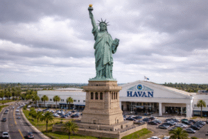 Ilustração gerada por inteligência artificial mostra réplica da Estátua da Liberdade em frente a uma loja da Havan, em Guaíba, no Rio Grande do Sul, sob céu nublado.