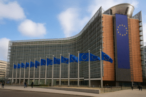 Fachada do edifício Berlaymont, sede da Comissão Europeia em Bruxelas, vista semiaérea em dia nublado, com bandeiras da União Europeia ao redor (imagem gerada por IA).