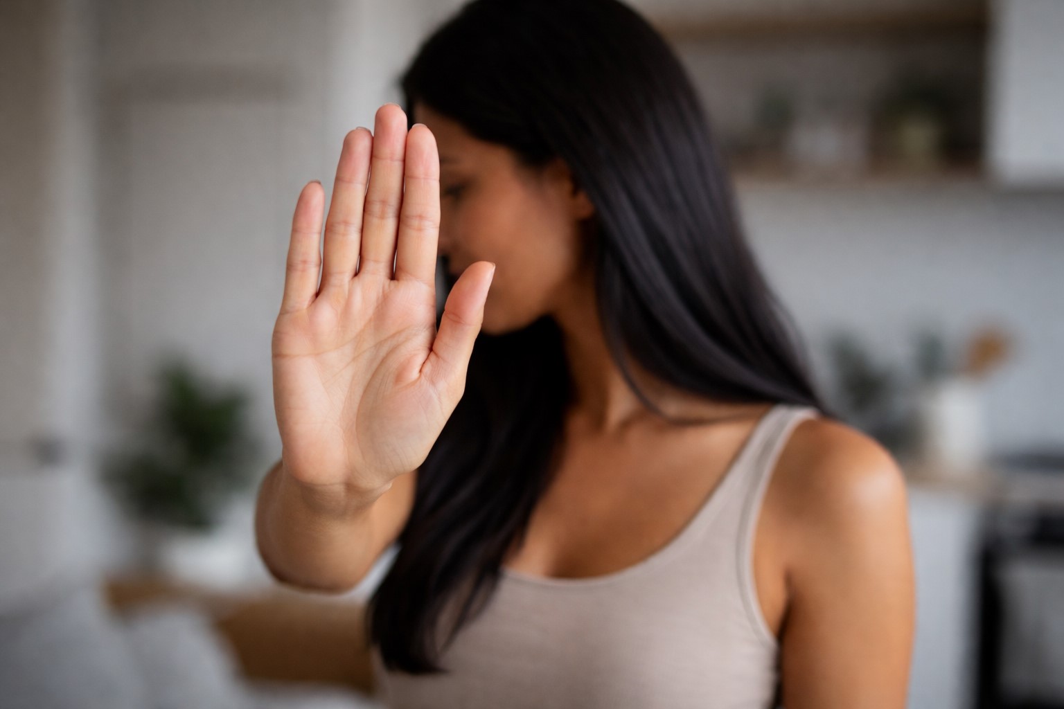 Mulher com a mão estendida em gesto de parada, em ambiente doméstico, representando situação de alerta e proteção.