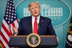 Donald Trump discursa em púlpito presidencial na Casa Branca, com bandeiras dos Estados Unidos e fundo oficial do governo norte-americano.