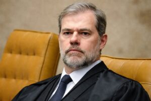 Ministro Dias Toffoli sentado em cadeira do Supremo Tribunal Federal, usando toga, terno escuro e gravata, em imagem institucional otimizada para publicação jornalística.