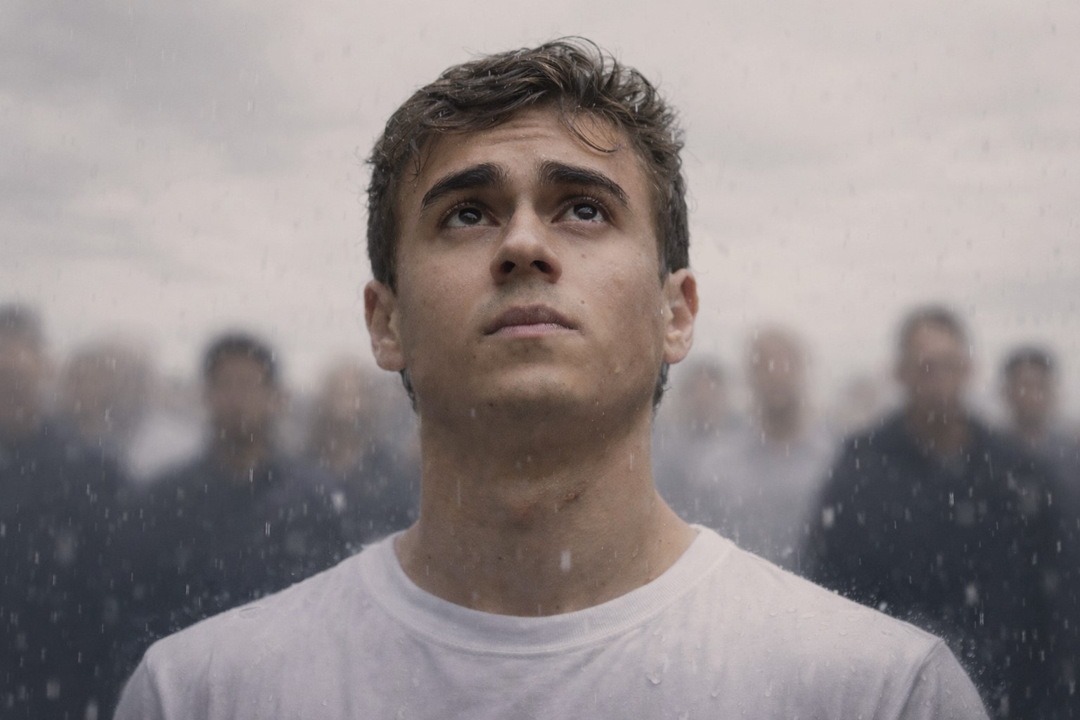 Deputado Nikolas Ferreira olha para cima sob chuva leve, com céu nublado e pessoas desfocadas ao fundo.