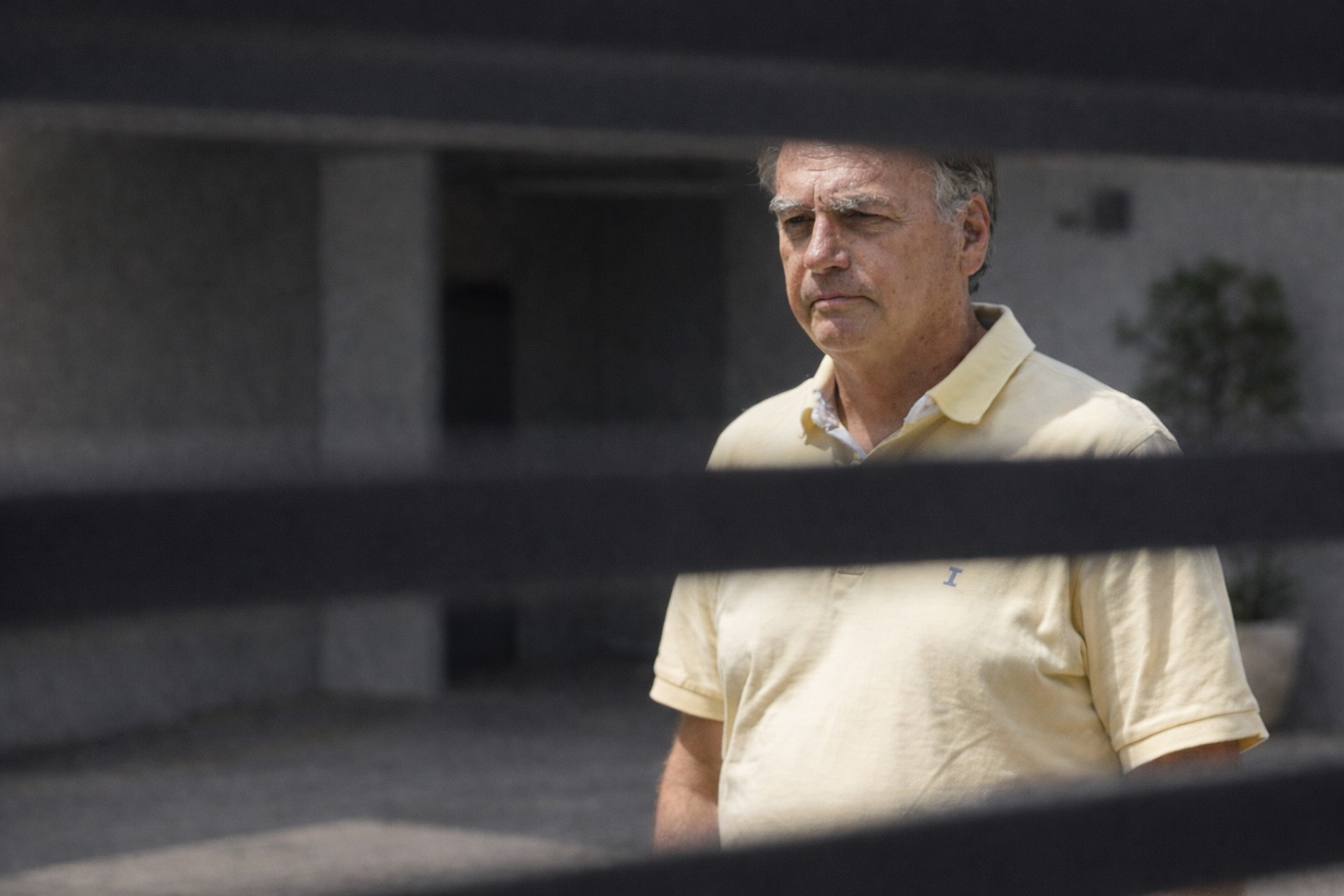 Imagem ilustrativa gerada por inteligência artificial mostra Jair Bolsonaro em ambiente residencial externo, visto através de portão com ripas horizontais.