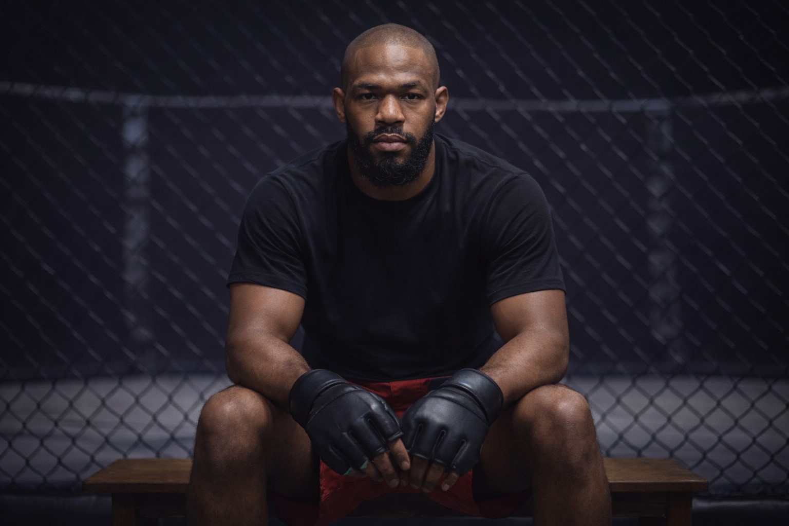Ilustração mostra Jon Jones sentado em banco diante de um octógono, usando luvas de treino e roupa esportiva, em ambiente de baixa iluminação.