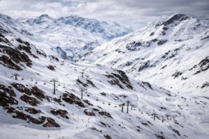 Imagem ilustrativa gerada por IA mostra os Alpes franceses nevados, com área de esqui e teleféricos em operação.