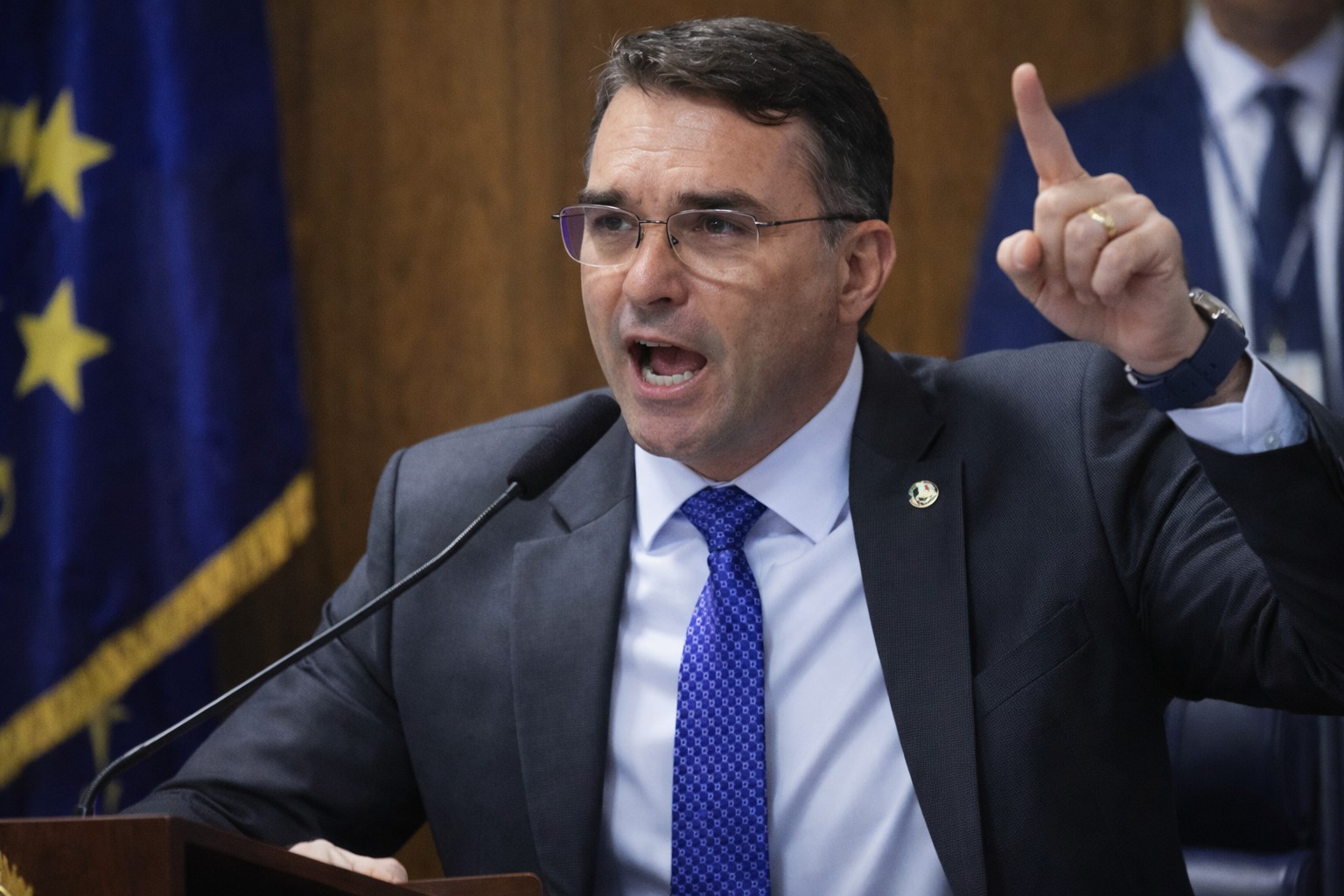 Imagem ilustrativa mostra o senador Flávio Bolsonaro discursando em púlpito político, em composição visual gerada por inteligência artificial.