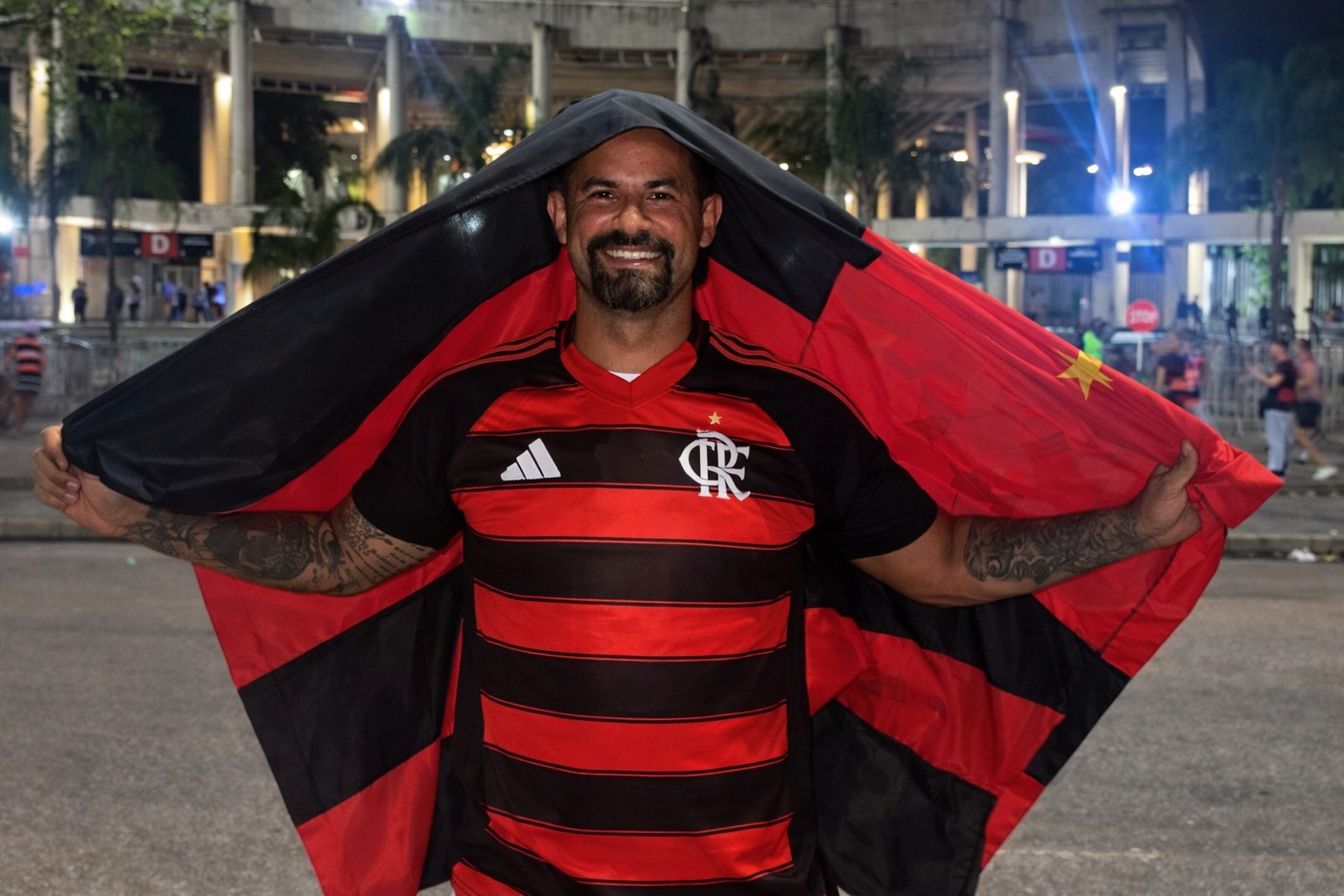 Goleiro Bruno aparece com camisa e bandeira do Flamengo na área externa do Maracanã, em imagem de reprodução otimizada por inteligência artificial.