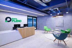 Recepção interna do Banco Pleno com logotipo na parede, balcão de atendimento e área de espera moderna; imagem original de divulgação do banco, otimizada por inteligência artificial para fins informativos.
