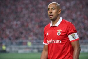 Imagem ilustrativa mostra o ex-zagueiro Luizão com uniforme do Benfica e faixa de capitão em campo, com arquibancada ao fundo; arte gerada por inteligência artificial para contextualização informativa.