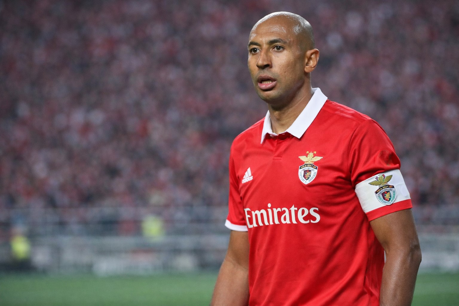 Imagem ilustrativa mostra o ex-zagueiro Luizão com uniforme do Benfica e faixa de capitão em campo, com arquibancada ao fundo; arte gerada por inteligência artificial para contextualização informativa.