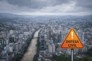 Vista semiaérea de Juiz de Fora sob chuva intensa, com placa simbólica de alerta da Defesa Civil em primeiro plano. Imagem ilustrativa gerada por IA.