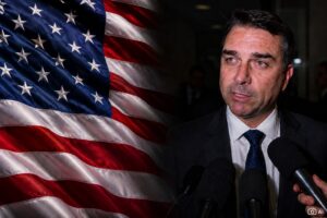Montagem fotográfica realista mostra Flávio Bolsonaro à direita, em ambiente de conversa com a imprensa, com microfones à frente, enquanto a bandeira dos Estados Unidos aparece à esquerda em composição visual de contexto jornalístico.