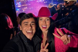 Registro fotográfico real de Nikolas Ferreira e Ana Castela na Festa do Peão de Barretos. Os dois aparecem sorrindo para a câmera em uma selfie feita em meio ao evento, com luzes coloridas e público ao fundo. A imagem teve a resolução otimizada por IA, sem alteração do conteúdo jornalístico do registro.