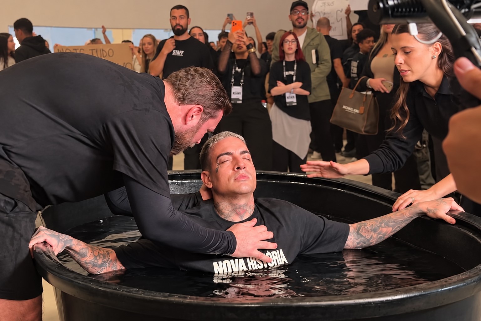 MC Guimê aparece dentro de uma piscina batismal durante cerimônia religiosa na Igreja Celeiro, em São Paulo, acompanhado pelo pastor e por participantes do culto.